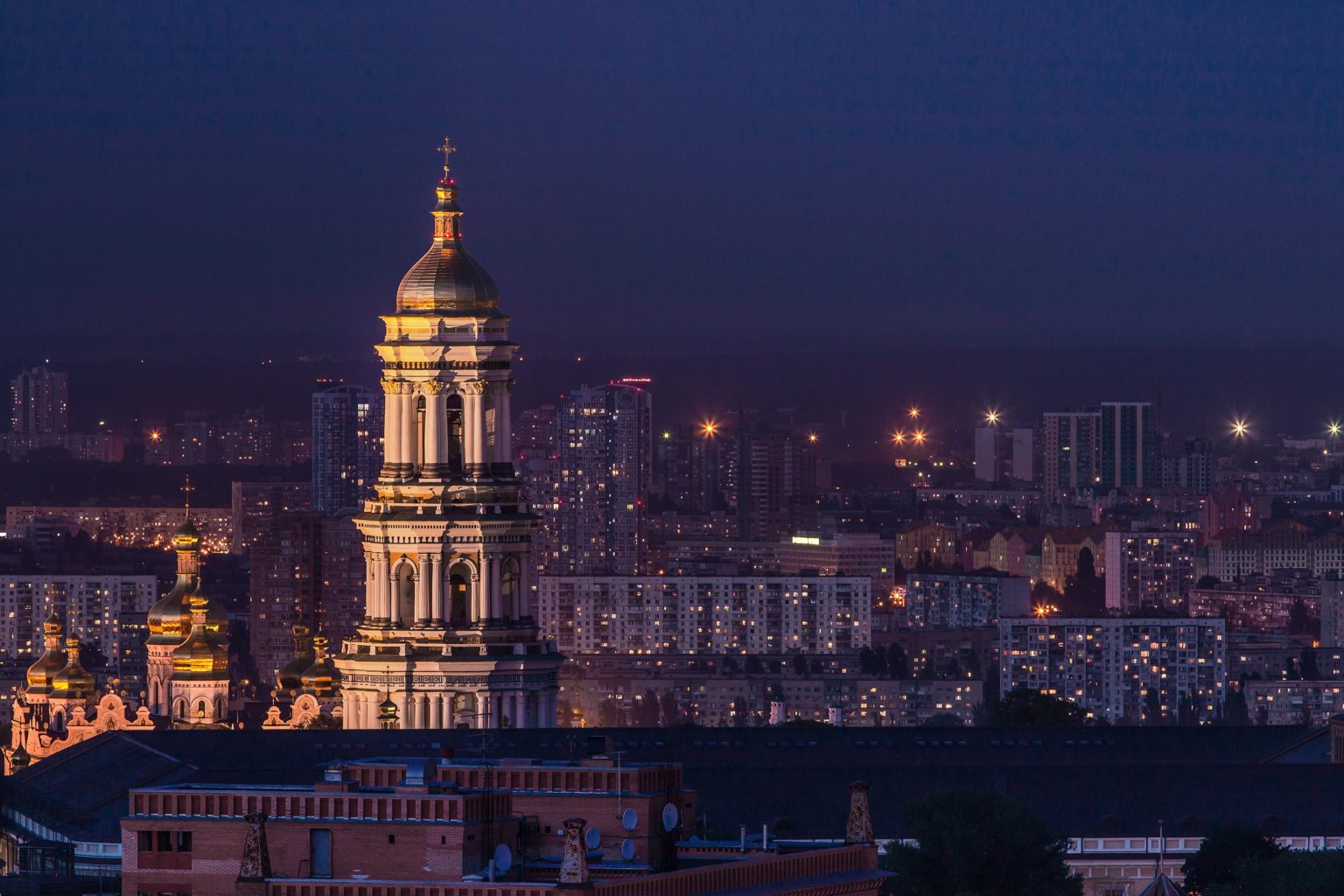 Nachtaufnahmeeines Kirchturms, im Hintergrund leuchten die Lichter der Stadt