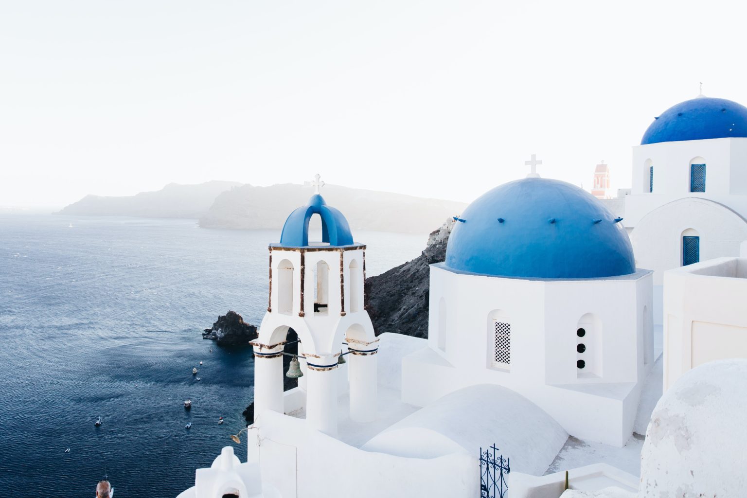 Weiß gekalkte Häuser mit strahlend blauen Dächern wurden am Felshang einer Insel erbaut. Foto: Unsplash/Jonathan Gallegos.