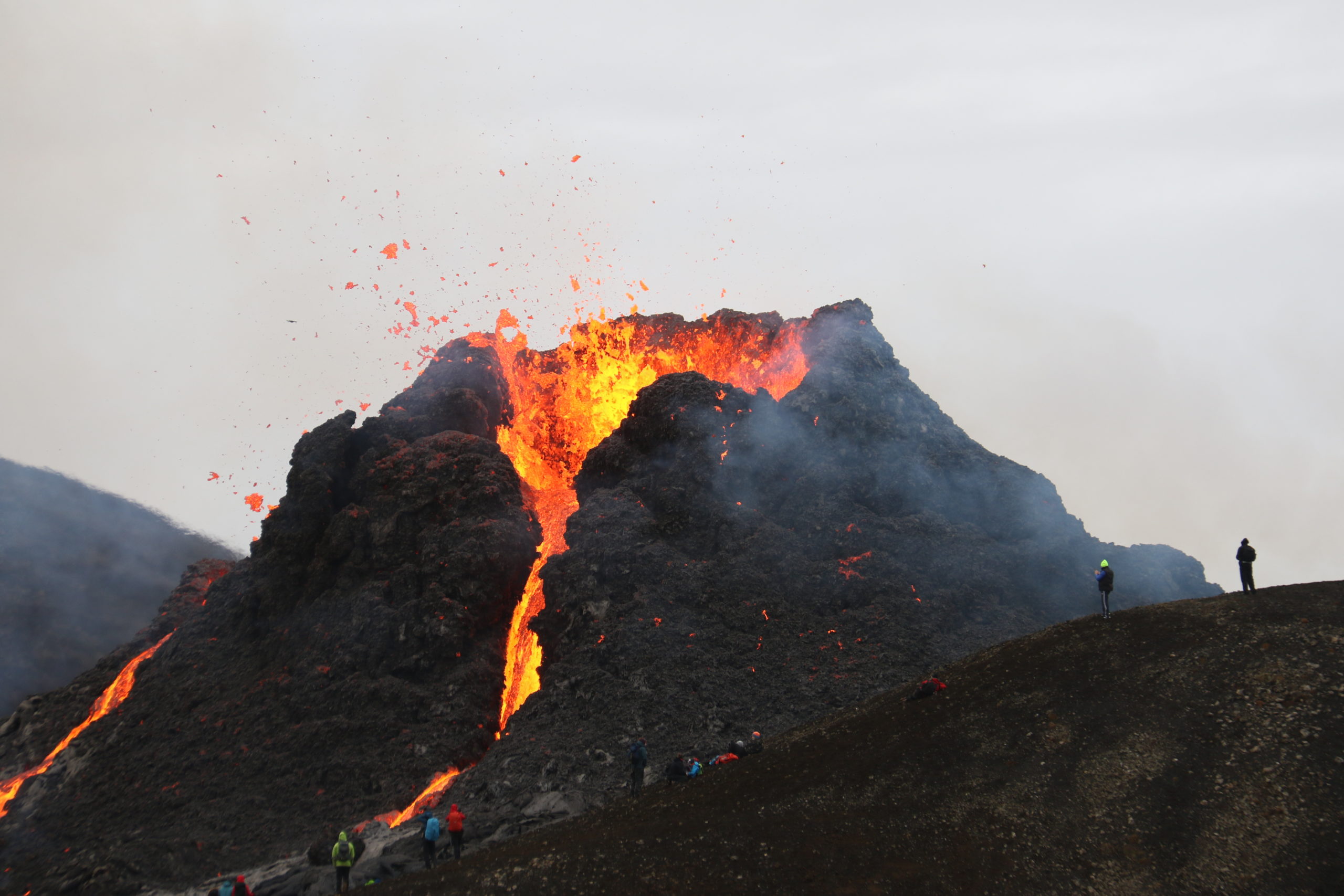 Orangen glühende Lava fließt aus einer Bergspitze, Menschen beobachten das Ganze