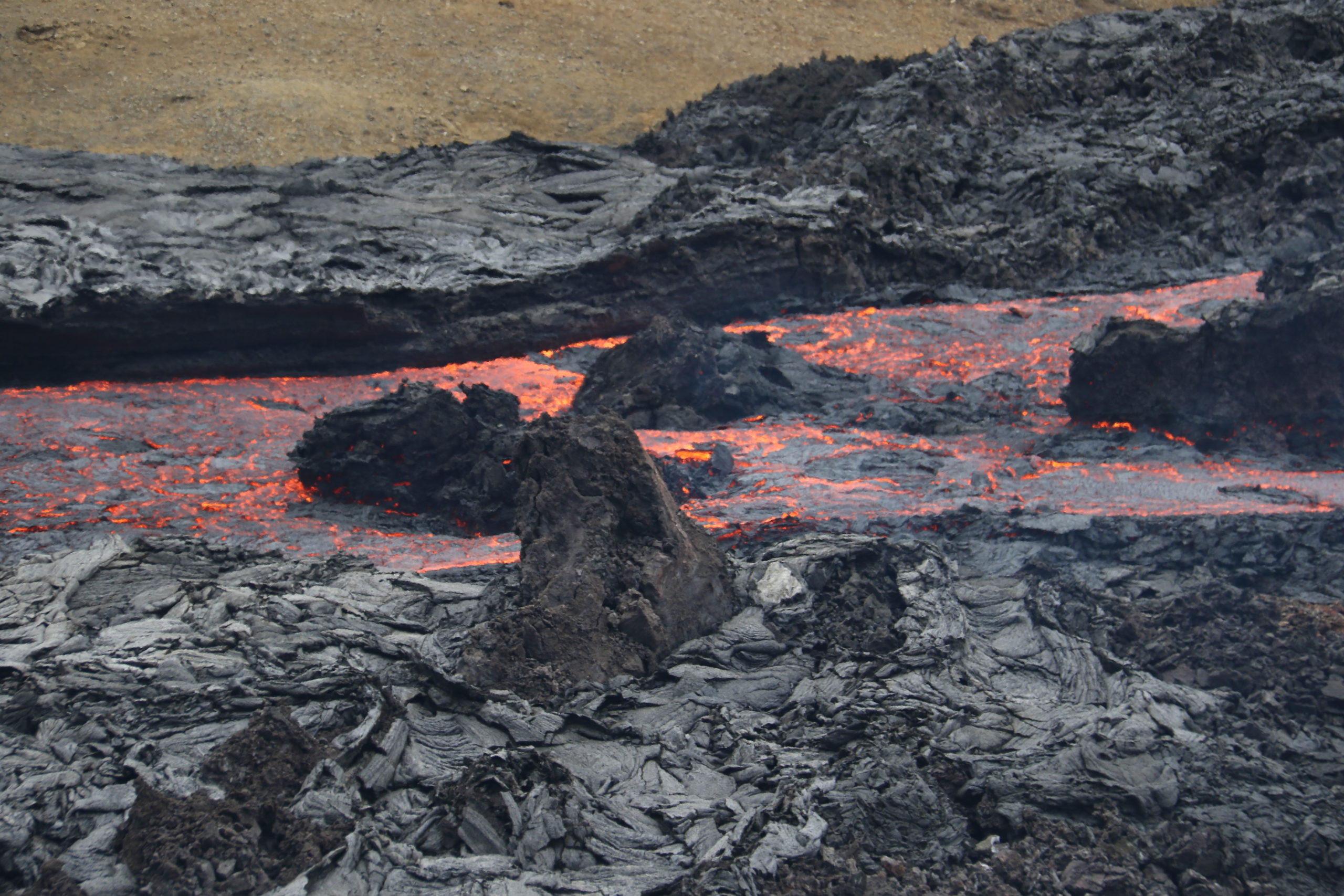 Lava fließt schwarz-orange durch schwarzen Schlamm.