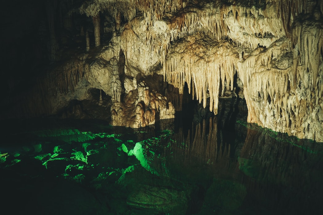 Eine Höhle voller runterhängender Zapfen und grünem Wasser