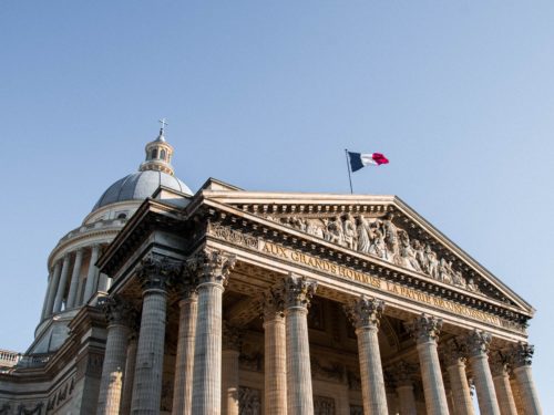 Ein altes Gebäude mit Säulen und einem Runddach, obendrauf die Französische Flagge.