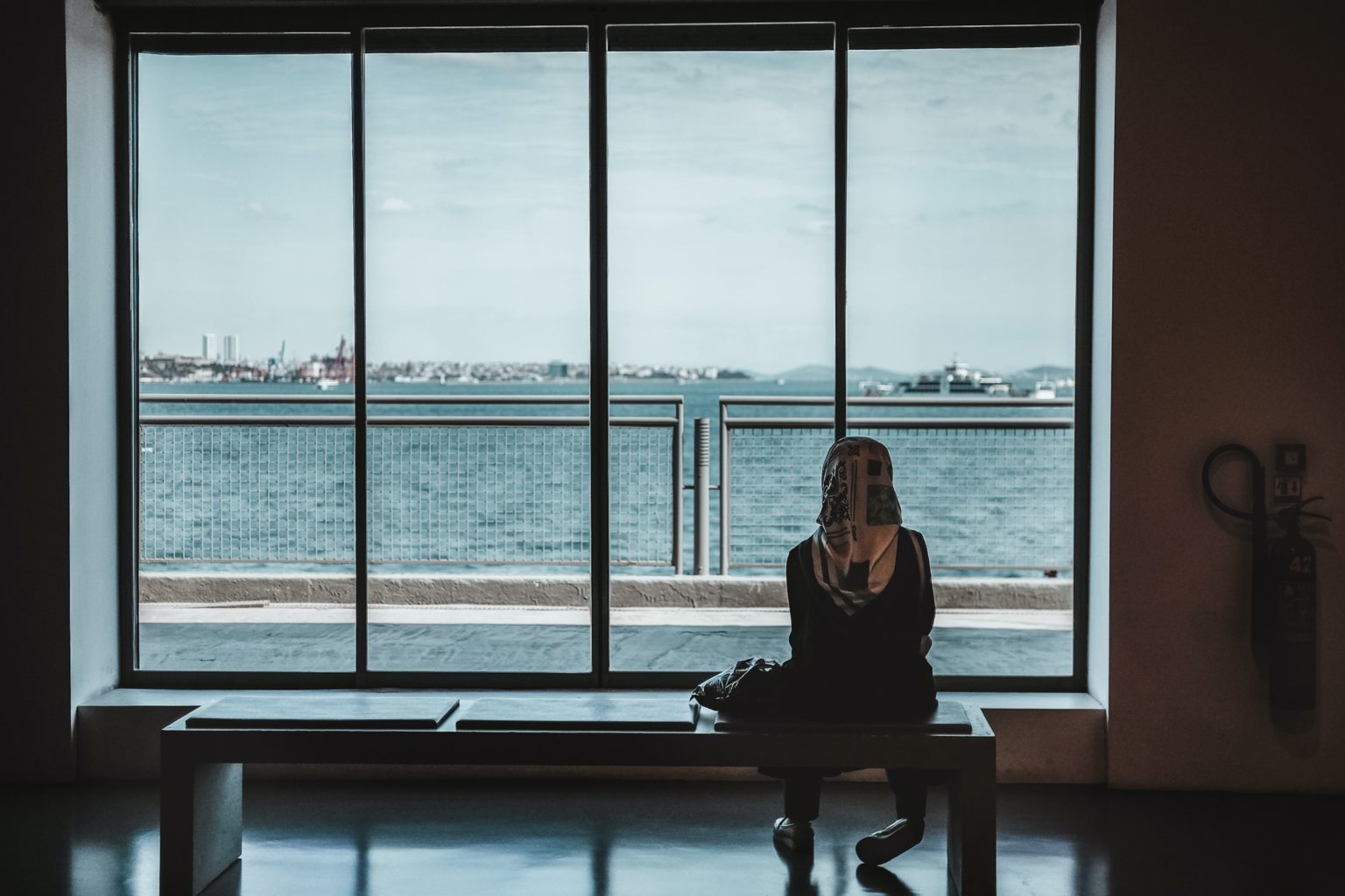 Eine Frau blickt von innen auf den Hafen und das Meer. Credits: Unsplash/Maria Teneva