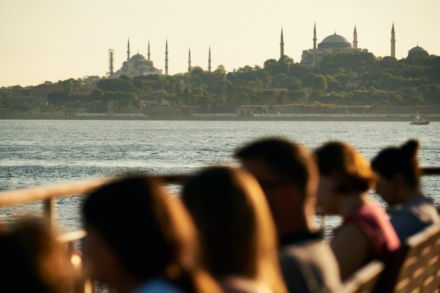 Menschen sitzen Wasser, im Hintergrundsind Türmchen und eine Moschee zu erkennen.