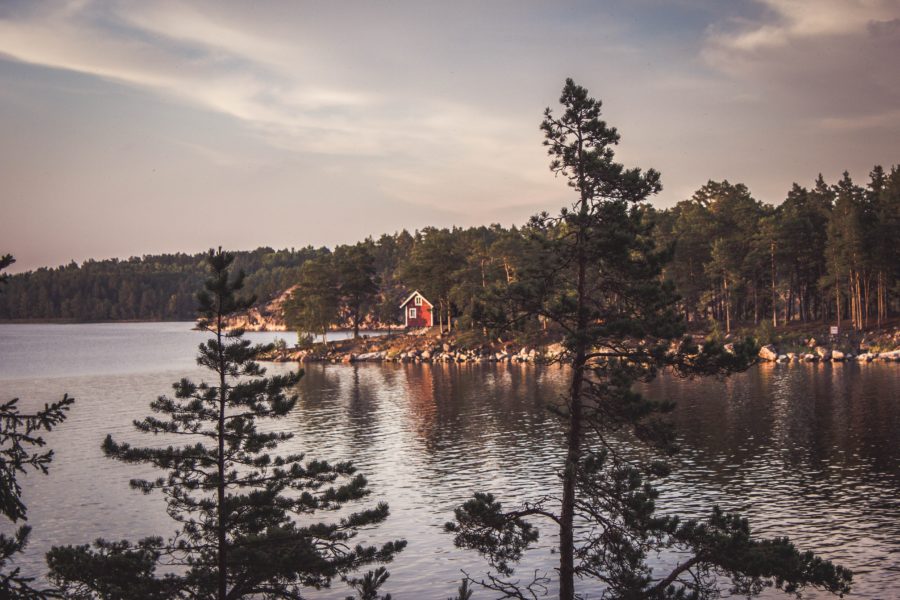 Auf einer Felseninsel steht ein rotes Holzhaus. Foto: Unsplash/Ines d'Anselme.