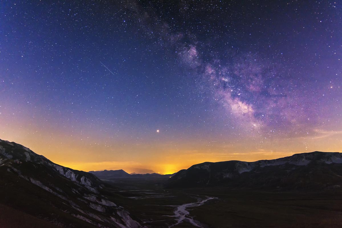 Im Vordergrund ein Bergpanorma bei Nacht, im Hintergrund einen Sternenhimmeln mit Milchstraße
