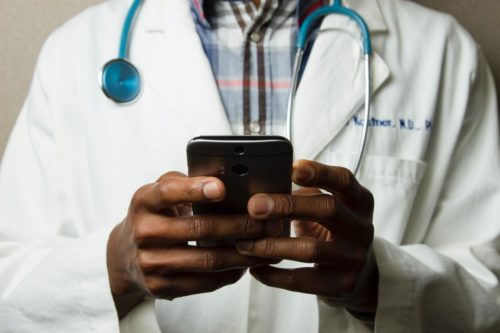 Mann im Arztkittel hält ein Smartphone in beiden Händen