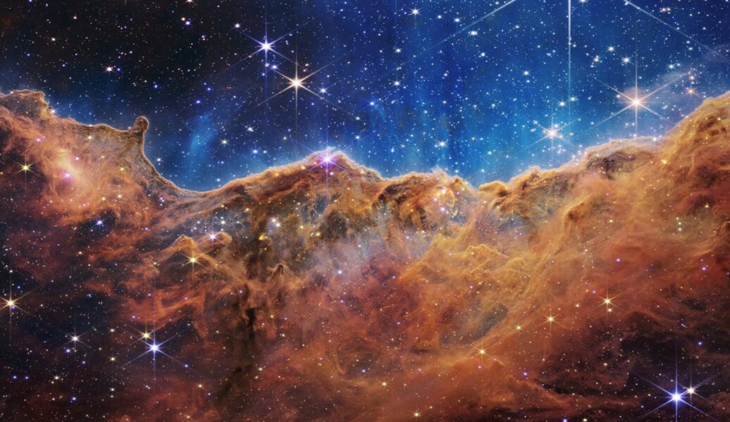Falschfarbendarstellung des Carina-Nebels. Im Vordergrund eine bräunliche Nebelwand, dahinter blauer Sternenhimmel